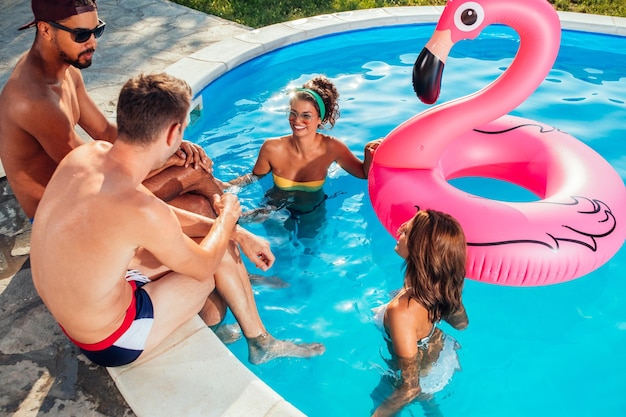 Photo de quatre amis qui traînent au bord de la piscine