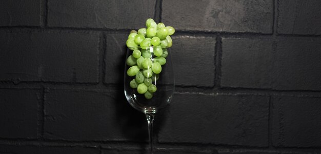 Photo de raisins verts dans le verre de vin, isolé sur le mur de briques noires.