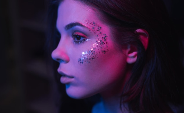 Photo rapprochée du visage d'une femme avec un maquillage intéressant la nuit à la fête avec une lumière violette mettant l'accent sur les paillettes