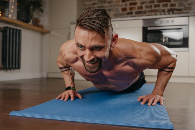 Une photo rapprochée d'un homme musclé avec une barbe qui fait des pompes sur un tapis de yoga dans son appartement le soir