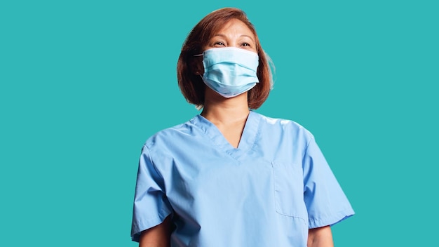 Une photo rapprochée d'une infirmière BIPOC joyeuse portant un masque de protection médicale, isolée sur un fond bleu du studio.