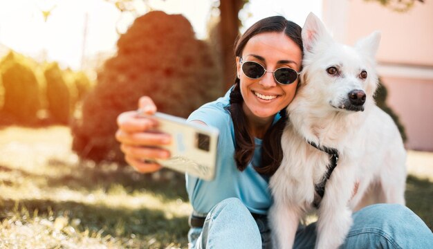 Une photo rapprochée d'une jeune fille souriante qui se prend un selfie avec son chien blanc à l'extérieur sur la pelouse Adoption sauvée compagnon d'abri animal de compagnie meilleur ami