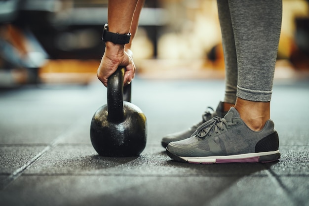 Photo recadrée d'une athlète féminine méconnaissable qui s'entraîne avec un kettlebell à la salle de sport.