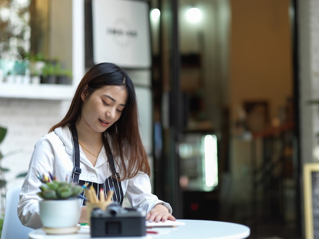 Photo recadrée de la belle artiste féminine avec tablier peinture sur table basse au café