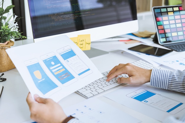 Photo recadrée des concepteurs front-end de démarrage de l'interface utilisateur UX UI développant la programmation et le codage d'applications mobiles à partir d'une disposition de prototype et de structure filaire. Concept de lieu de travail pour développeur d'applications mobiles.
