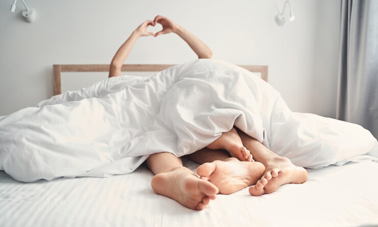 Photo photo recadrée d'un couple nouvellement marié en forme de coeur avec les mains au lit