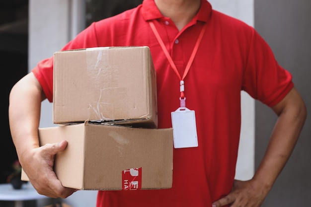 Photo recadrée d'un coursier masculin en uniforme rouge tenant une boîte en carton à l'extérieur du bureau.