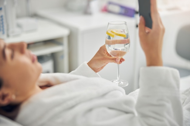 Photo recadrée d'une dame de race blanche tenant un téléphone portable et de l'eau citronnée dans ses mains