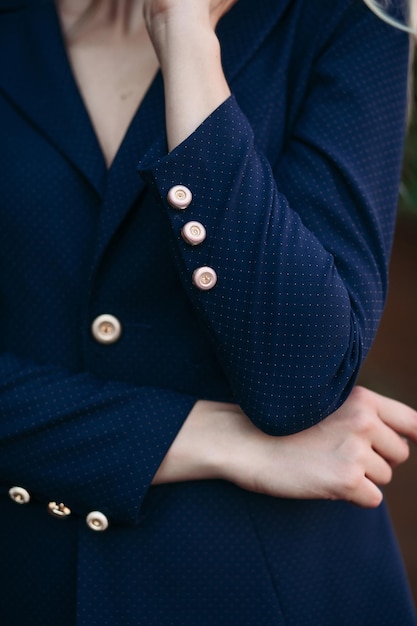 Photo recadrée d'une élégante femme d'affaires blonde magnifique dans une veste et un pantalon noir foncé coûteux avec des boutons dorés sur les manches Elle est debout, les bras croisés