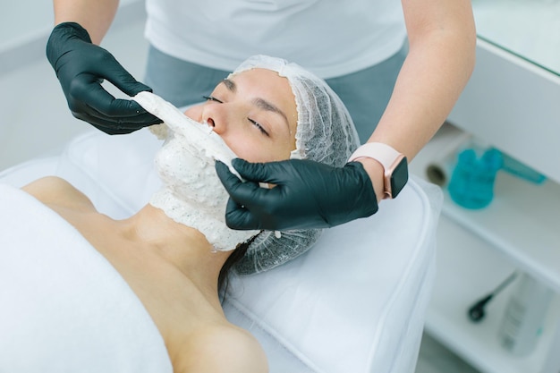 Photo recadrée d'un employé d'une clinique de beauté enlevant le masque d'alginate du visage d'une femme