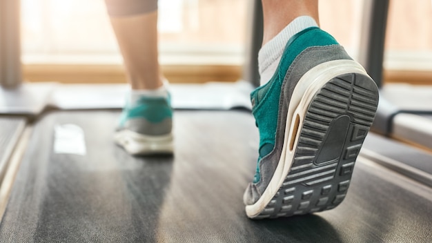 Photo recadrée d'entraînement cardio d'une femme en chaussures de sport courant sur un tapis roulant au sport de gym