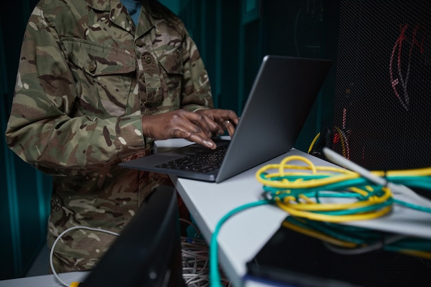 Photo recadrée d'une femme afro-américaine méconnaissable portant un uniforme militaire utilisant un ordinateur lors de la configuration du réseau dans la salle des serveurs, espace de copie