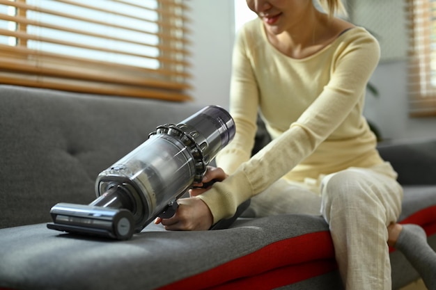 Photo recadrée d'une femme au foyer du millénaire nettoyant un canapé avec un aspirateur sans fil pour éliminer les germes et la saleté