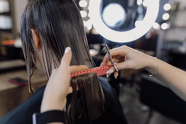 Photo recadrée d'une femme coiffeuse faisant une coiffure se brossant les cheveux mouillés avec un peigne rose tenant des ciseaux