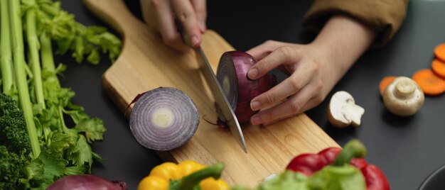 Photo recadrée de femme cuisinière coupant l'oignon rouge frais sur un bloc