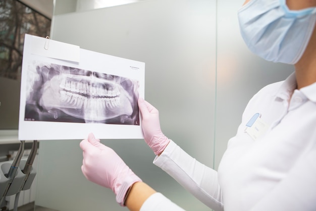 Photo recadrée de femme dentiste portant un masque médical montrant une radiographie de la mâchoire à l'appareil photo