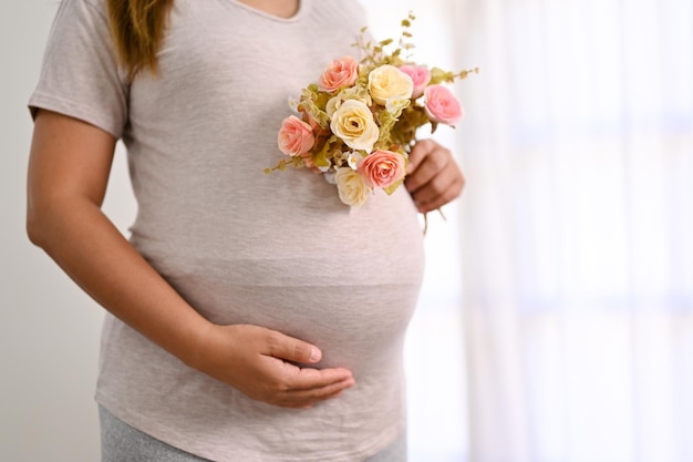 Photo recadrée d'une femme enceinte tenant un beau bouquet de fleurs et touchant son ventre