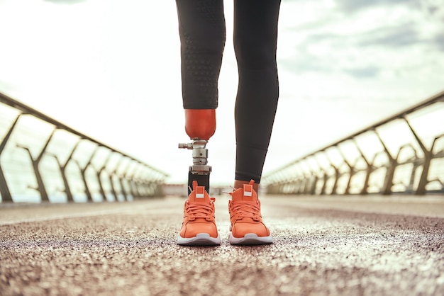 Photo recadrée d'une femme handicapée avec une jambe prothétique en tenue de sport debout sur le pont