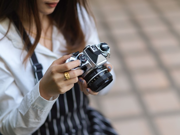 Photo recadrée de femme photographe avec tablier vérifiant la photo sur un appareil photo numérique tout en prenant une photo au café