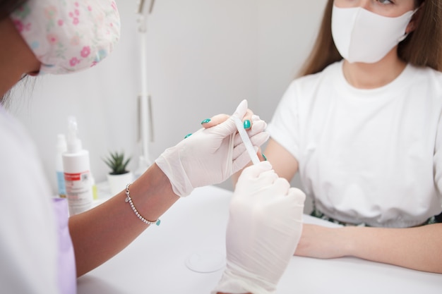 Photo recadrée d'une femme et de sa manucure portant des masques faciaux tout en faisant des ongles