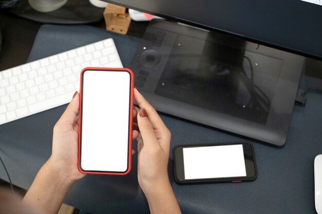 Photo recadrée d'une femme tenant un téléphone intelligent avec écran blanc sur son lieu de travail.