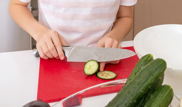 Photo recadrée de fille couper le concombre avec un couteau sur une table dans la cuisine