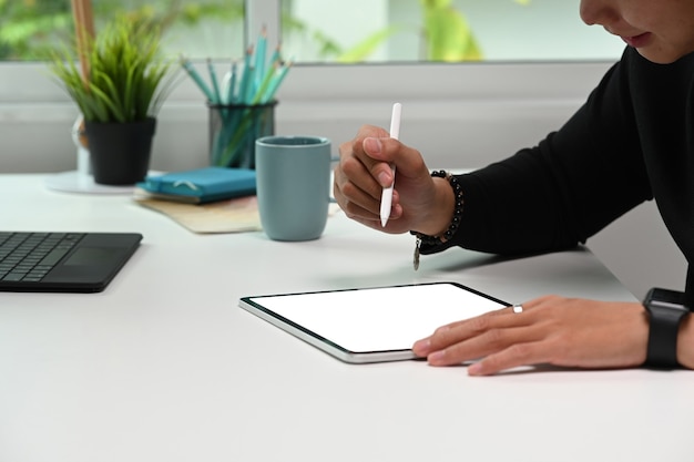 Photo recadrée d'un graphiste éditant une photo avec une tablette numérique sur un bureau blanc.