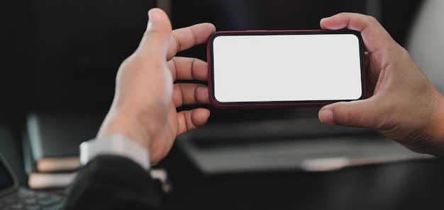 Photo recadrée d'homme d'affaires professionnel tenant un écran blanc dans une pièce de bureau moderne sombre