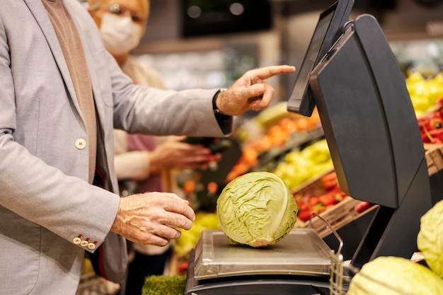 Photo recadrée d'un homme âgé mesurant le chou sur une balance au supermarché