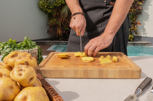 Photo recadrée d'un homme coupant des pommes de terre sur une planche de bois