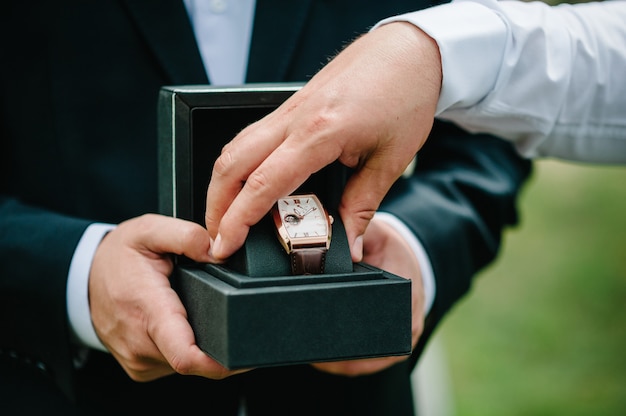 Photo recadrée d'un homme portant un costume élégant et tenant une montre-bracelet. Main d'homme avec une montre de luxe élégante et chère avec un bracelet en cuir sur un fond de nature.