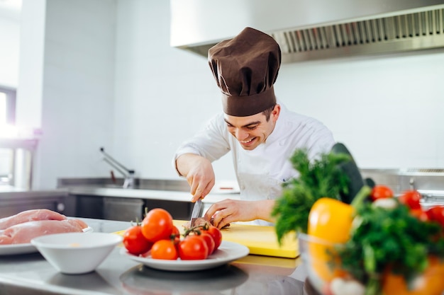 Photo recadrée d'un jeune chef masculin coupant la viande dans une cuisine professionnelle