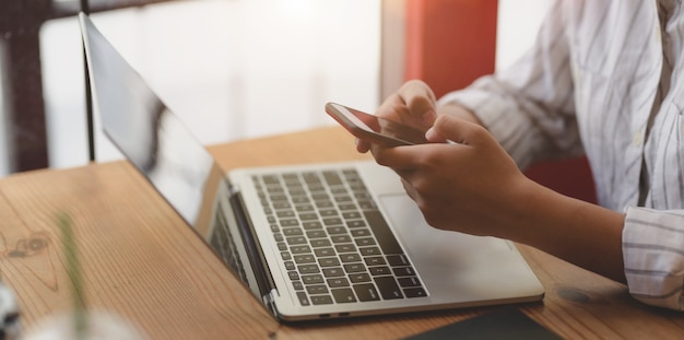 Photo recadrée de jeune femme d'affaires détenant un smartphone alors qu'il travaillait sur un ordinateur portable