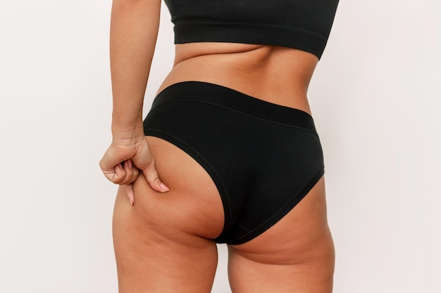 Photo recadrée d'une jeune femme bronzée en culotte noire saisissant la peau sur sa fesse avec un excès de graisse