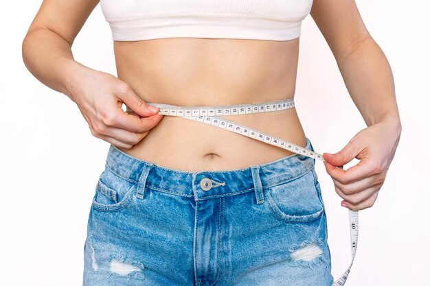 Photo recadrée d'une jeune femme mince en jeans mesurant sa taille avec un centimètre