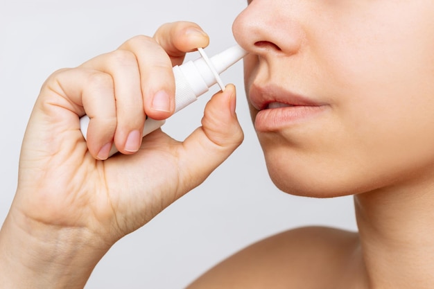 Photo recadrée d'une jeune femme de race blanche utilisant un spray nasal pour l'écoulement nasal et la congestion