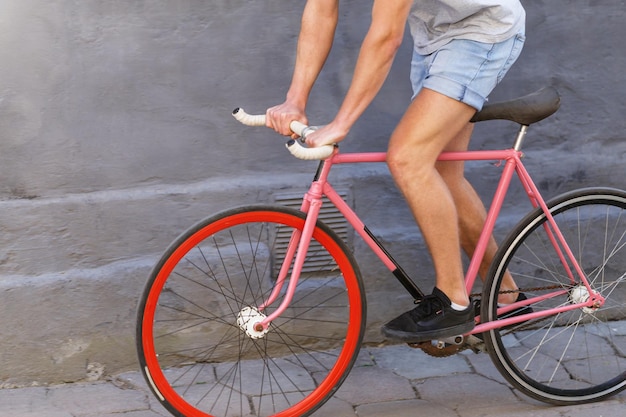 Photo recadrée d'un jeune homme caucasien en short en jean tôt le matin à vélo à l'extérieur