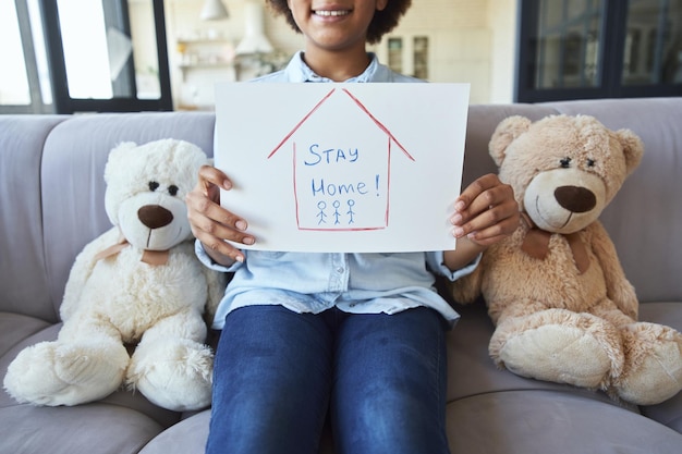 Photo recadrée d'une jolie adolescente métisse dans des vêtements décontractés souriant à la caméra et tenant rester à la maison