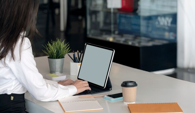 Photo recadrée de main de femme tapant sur le clavier de la tablette alors qu'il était assis au bureau, écran vide pour la conception graphique.