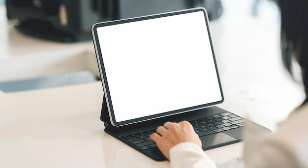 Photo recadrée de main de femme tapant sur le clavier de la tablette alors qu'il était assis à la table, écran vide pour la conception graphique.