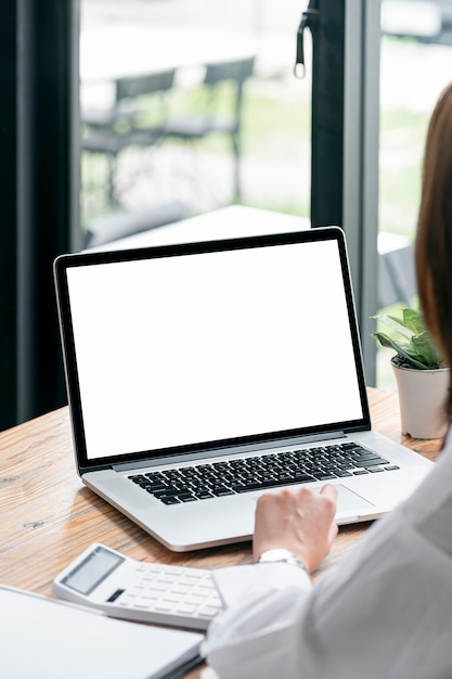 Photo recadrée d'une main de femme travaillant sur un ordinateur portable, maquette d'ordinateur portable à écran blanc pour l'affichage du produit, vue verticale.