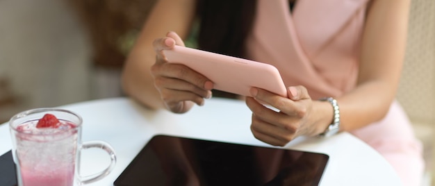 Photo recadrée de mains féminines tenant un smartphone horizontal tout en vous relaxant dans un café