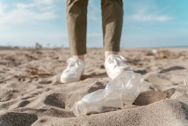 Photo photo recadrée d'un militant écologiste debout sur le sable devant une bouteille en plastique jetée