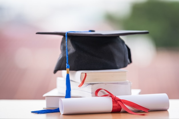 Photo recadrée d'un mortier de chapeau de graduation universitaire et d'un certificat de diplôme sur la table