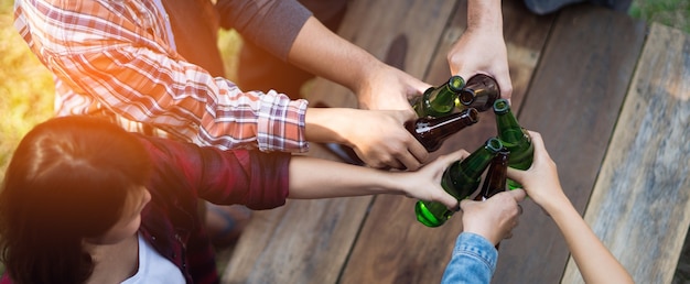 Photo recadrée de personnes tenant des verres à bière célébrant la fête de camping d'été en plein air. Amis tintant une bouteille de bière pendant le camping en plein air
