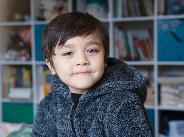 Photo recadrée d'un petit enfant portant des vêtements chauds pleins assis sur le lit en regardant la caméra avec un visage souriant, un enfant en bonne santé se réveillant le matin avec un visage heureux.