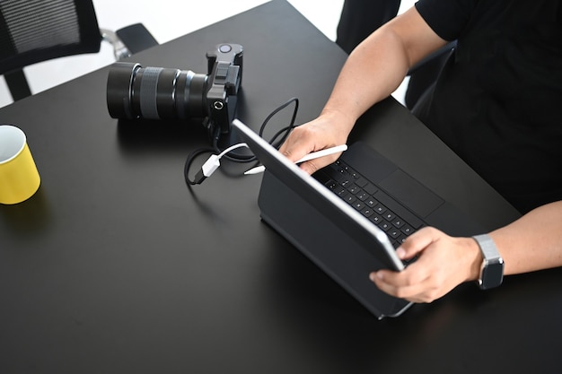 Photo recadrée d'un photographe masculin retouche des photos avec une tablette informatique dans son espace de travail créatif.