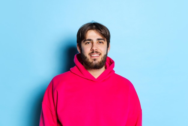 Photo recadrée en studio d'un jeune homme souriant regardant la caméra et posant isolé sur fond bleu