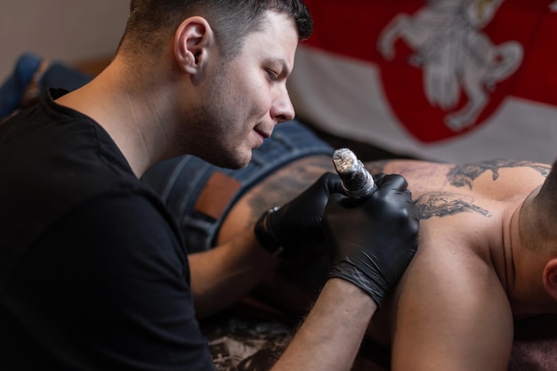 photo recadrée d'un tatoueur en gants travaillant sur le tatouage sur le corps dans le salon