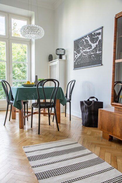 Photo réelle de l'intérieur de la salle à manger blanche avec table en bois de lampe en verre affiche carte avec citrons frais et chaises noires et tapis sur parquet à chevrons